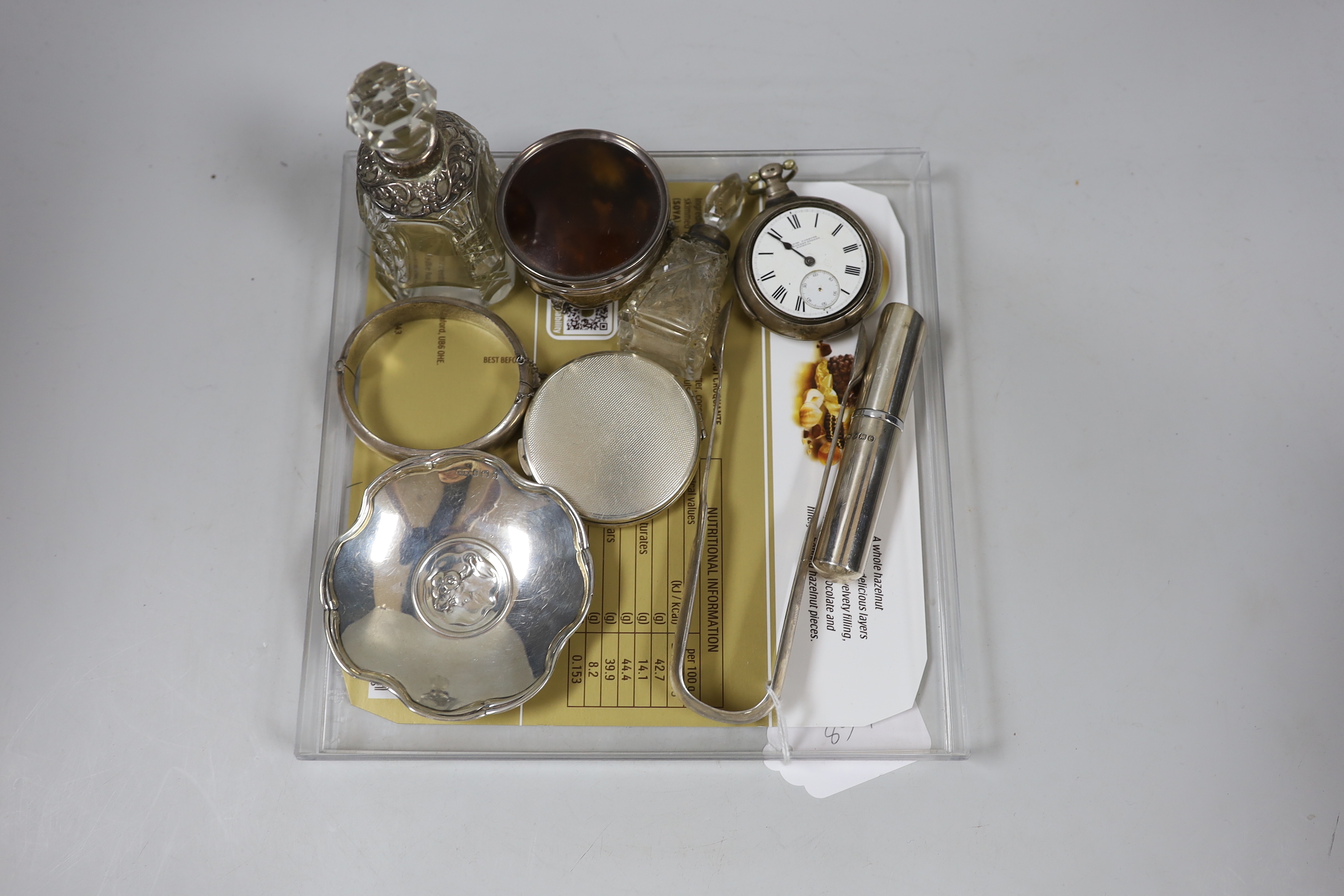 Sundry silver including a George V tortoiseshell mounted trinket box, diameter 6cm, two mounted glass scent bottles, modern atomiser, tongs, dish, compact, bangle and a verge pocket watch.